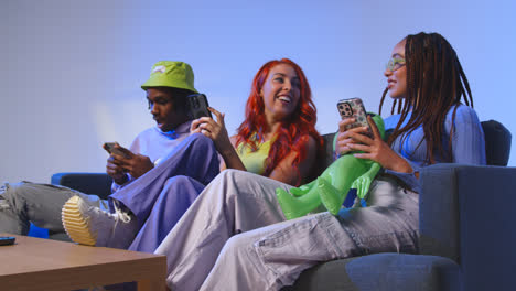 Studio-Shot-Of-Group-Of-Young-Gen-Z-Friends-Sitting-On-Sofa-Gaming-And-Using-Social-Media-On-Mobile-Phones-1